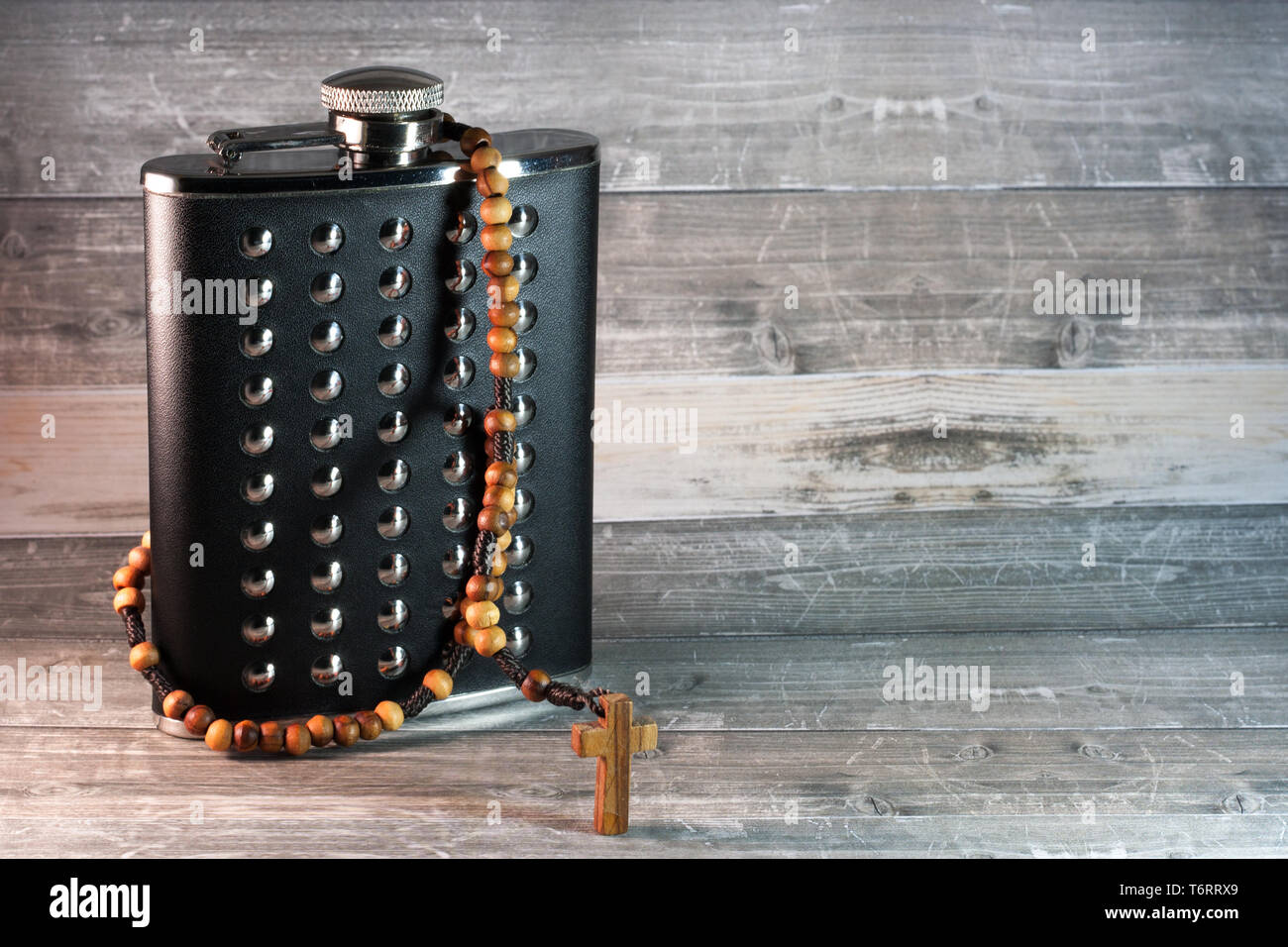 Wooden rosary wrapped around a standing, black leather hip flas with some stainless steel elements Stock Photo