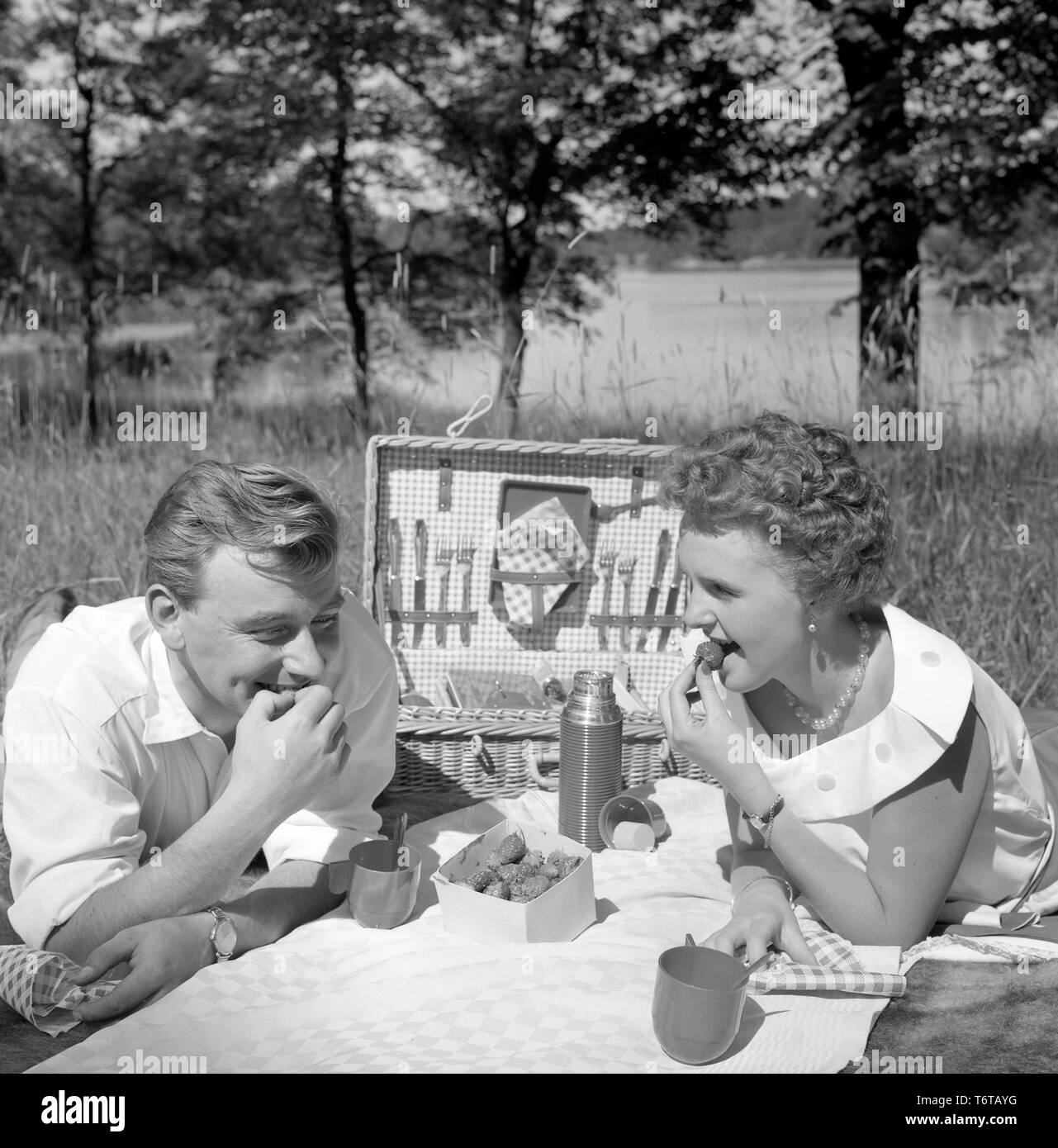 Picnic in the 1950s. A young couple are enjoying a sunny day. They have packed their food and drinks in the practical picnic case. They are eating fresh strawberries. Sweden 1956 Stock Photo