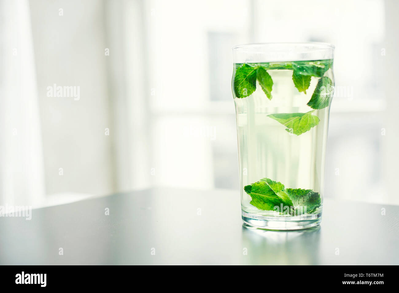 Peppermint water (a glass of water with fresh mint leaves). Soft tones with faded filter and natural light background. RF healthy lifestyle concept. Stock Photo