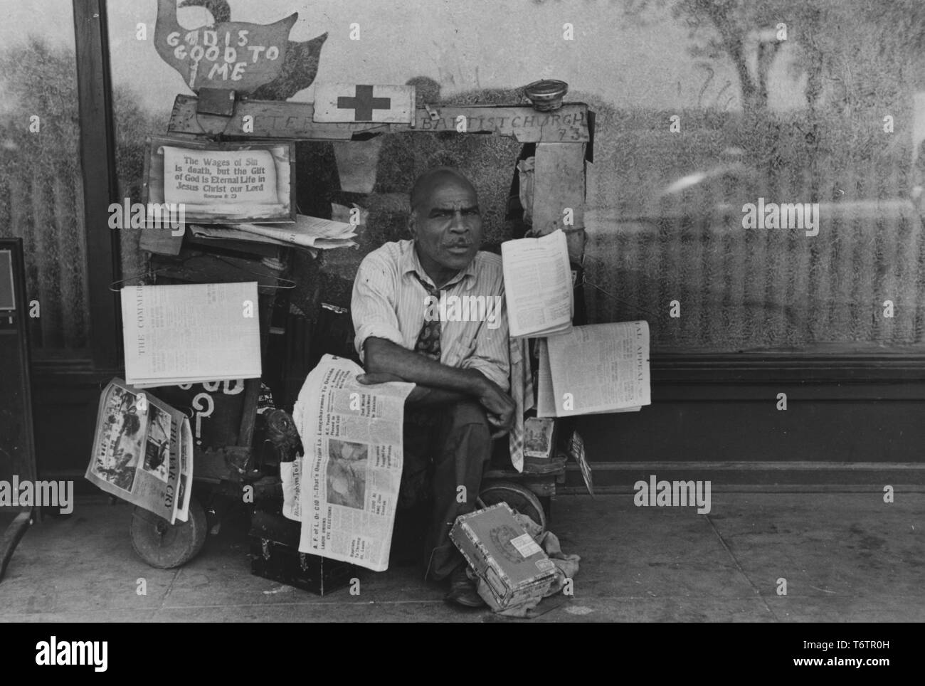 Photograph of African American man sitting on his newsstand cart surrounded by newspapers, Memphis, Tennessee, 1938. From the New York Public Library. () Stock Photo