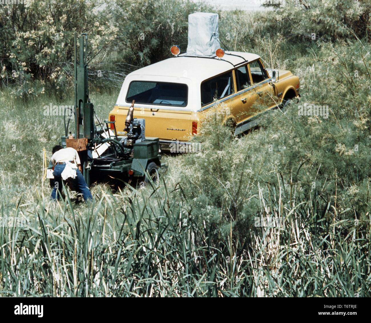 Male geologist, from the back, bending over to check the results of an  aerial radiometric and magnetic survey unit attached to the back of a  station wagon, Kellogg, Idaho, 1975. Image courtesy