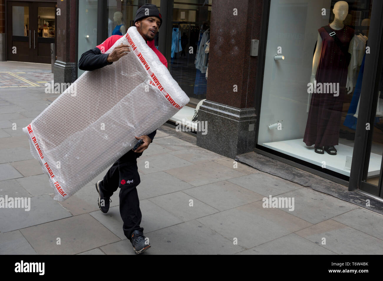 A courier with dpd carries a package wrapped in bubble wrap along Long
