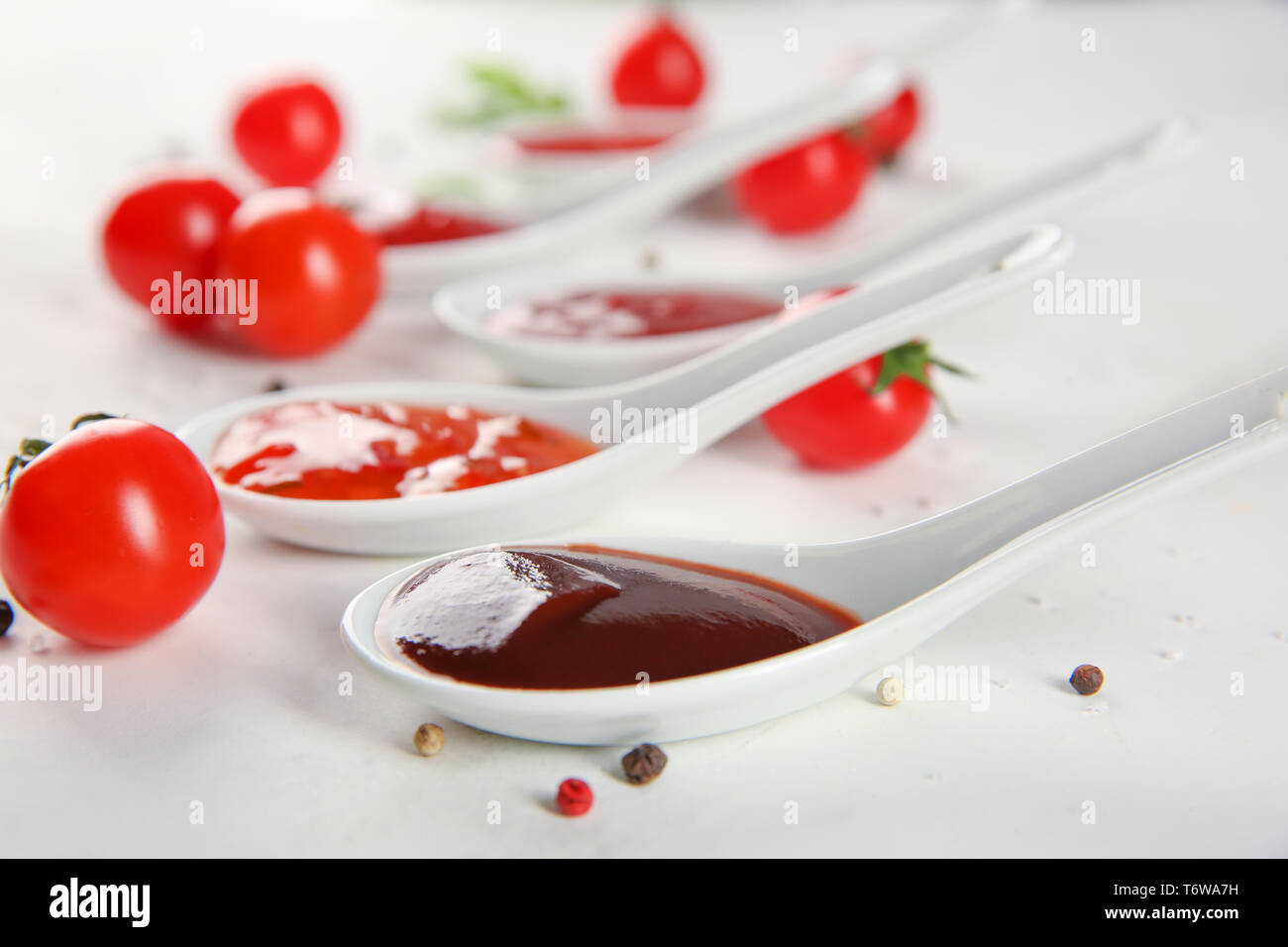 Spoons with red sauces and cherry tomatoes on light background Stock Photo