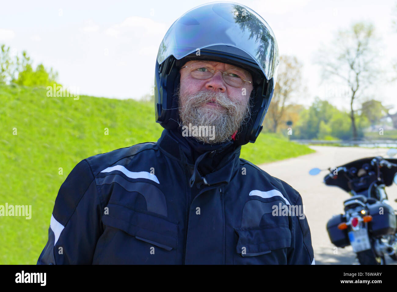 Mann mit langem Bart, Brille und Motorradhelm, steht am Ufer des Rhein Stock Photo