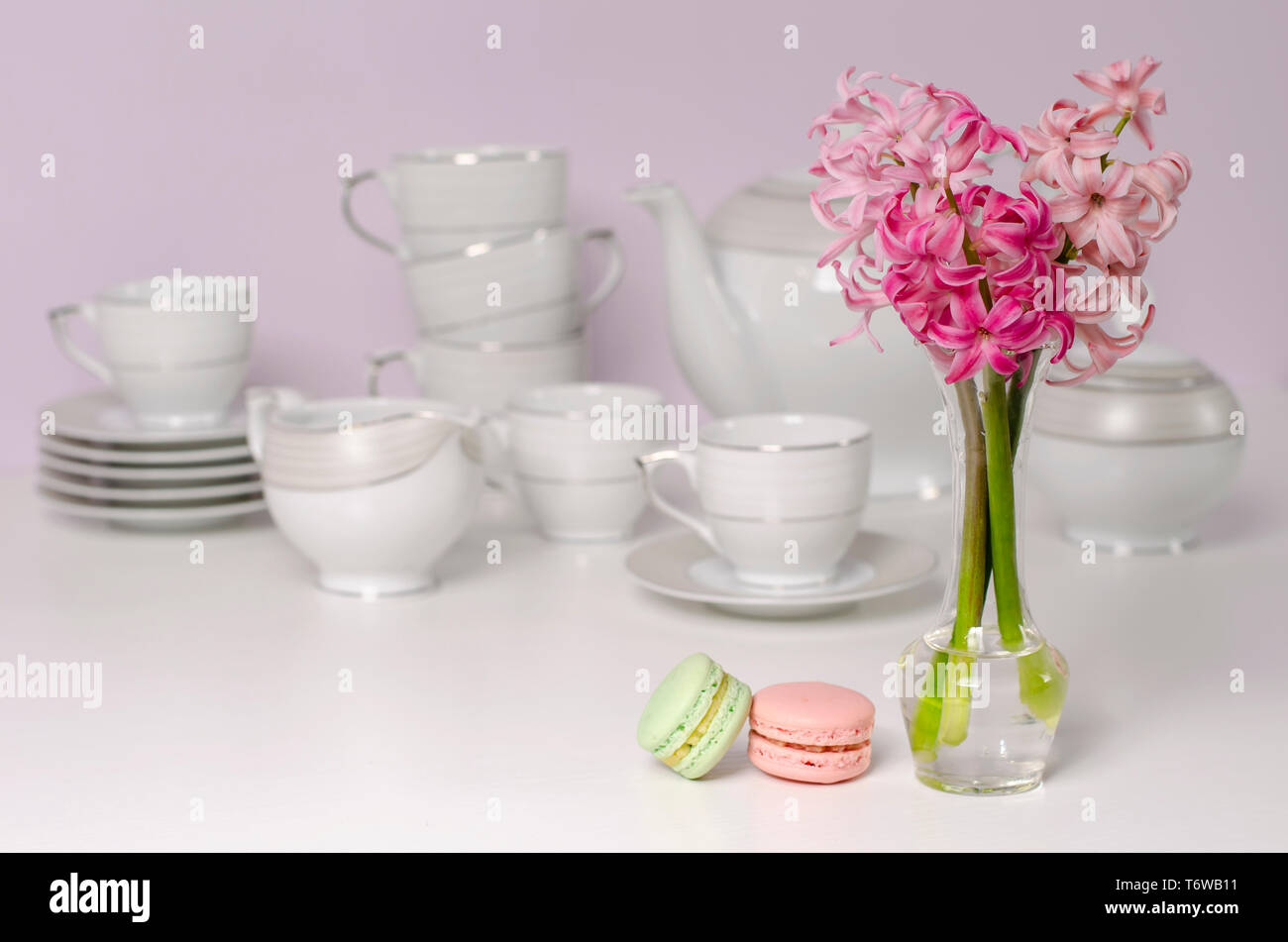 Two macaroons and transparent vase with pink hyacinth flowers on porcelain coffee set background. Selective focus. Tableware concept. Copy space. Stock Photo