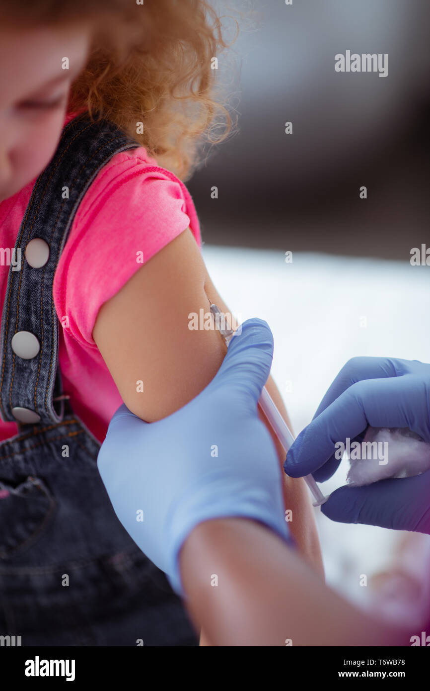 Pediatrician wearing blue gloves making injection for girl Stock Photo
