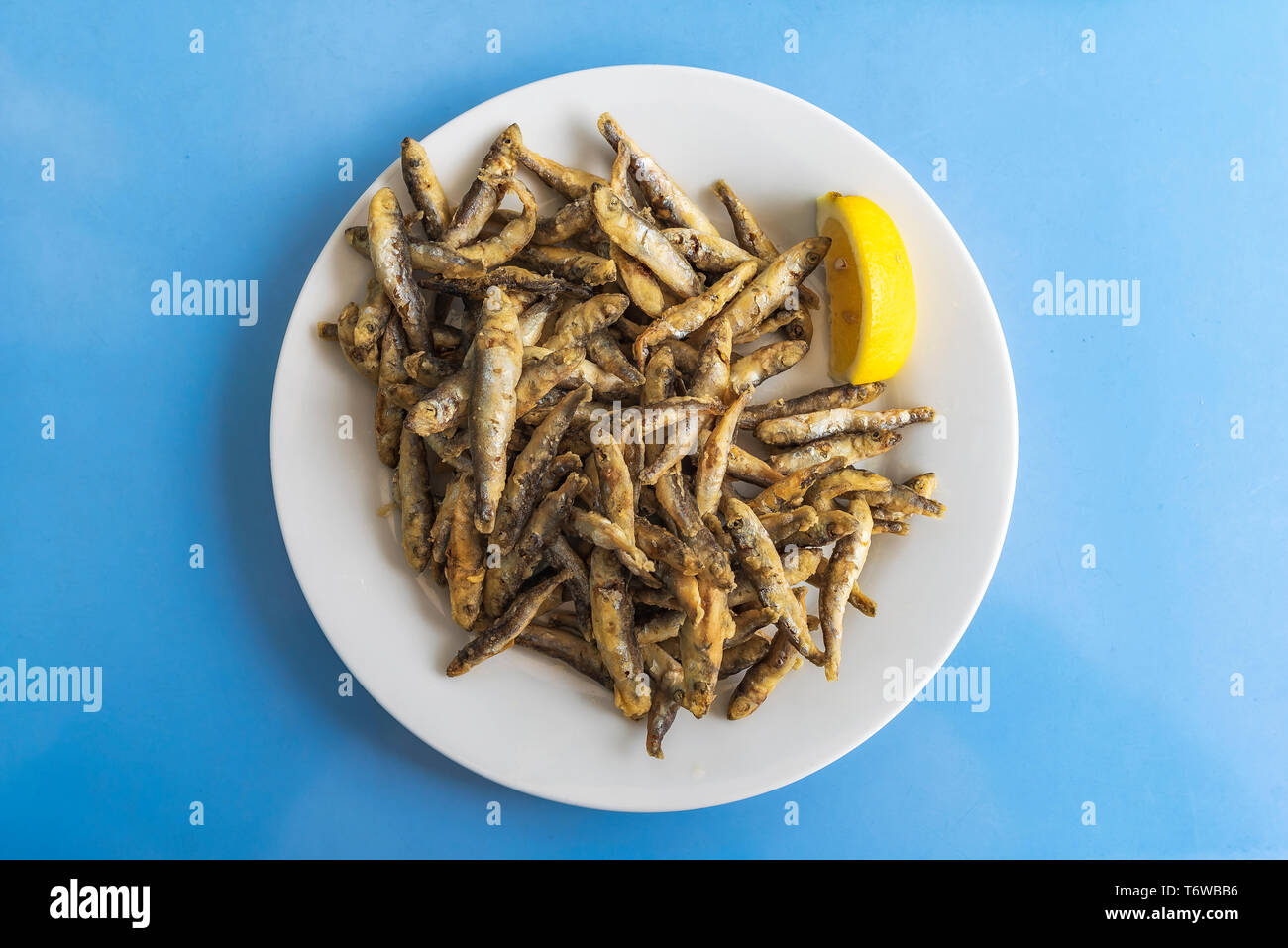 Fried sprat with lemon in white plate on blue table Stock Photo