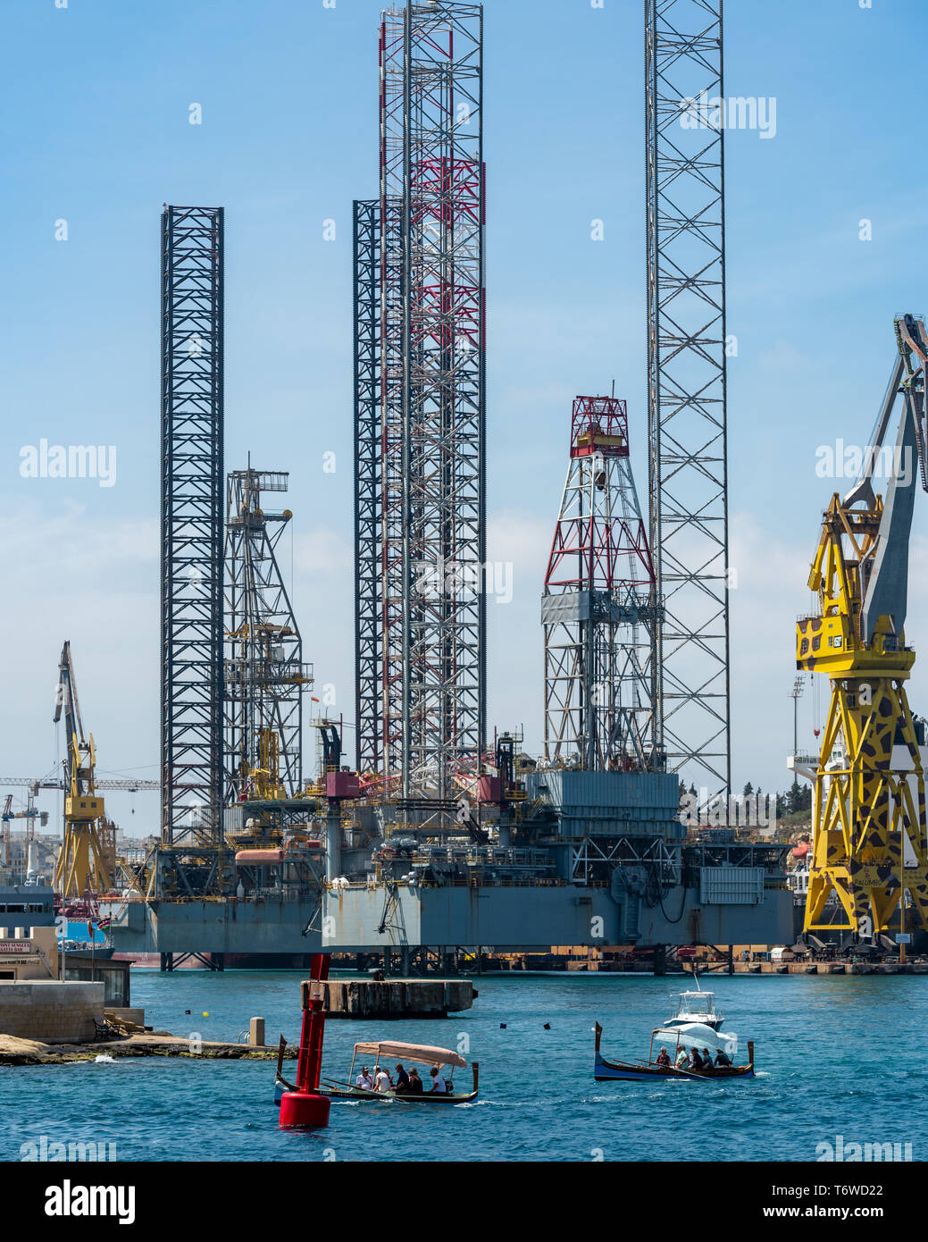 Traditional Dghajsa tal-Pass boats carry tourists past a large semi submersible drilling rig moored by Dock 6 of Valletta's Palumbo Shipyard Stock Photo