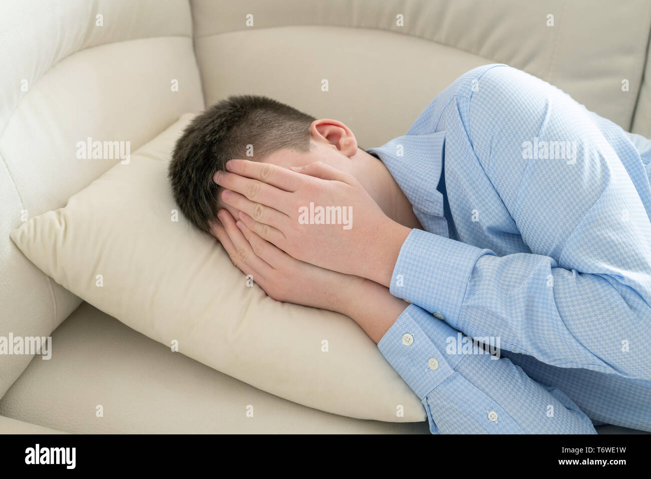 Depressed Teenager Lying On Couch Covering His Face With His Hands