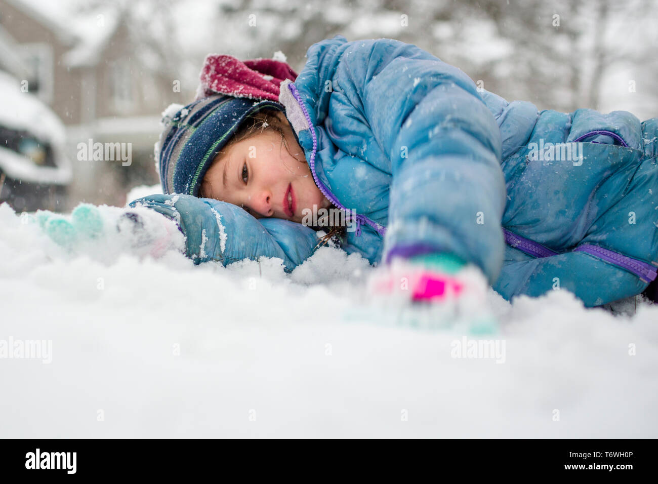 Portrait of a small child laying down on the ground in falling snow Stock Photo