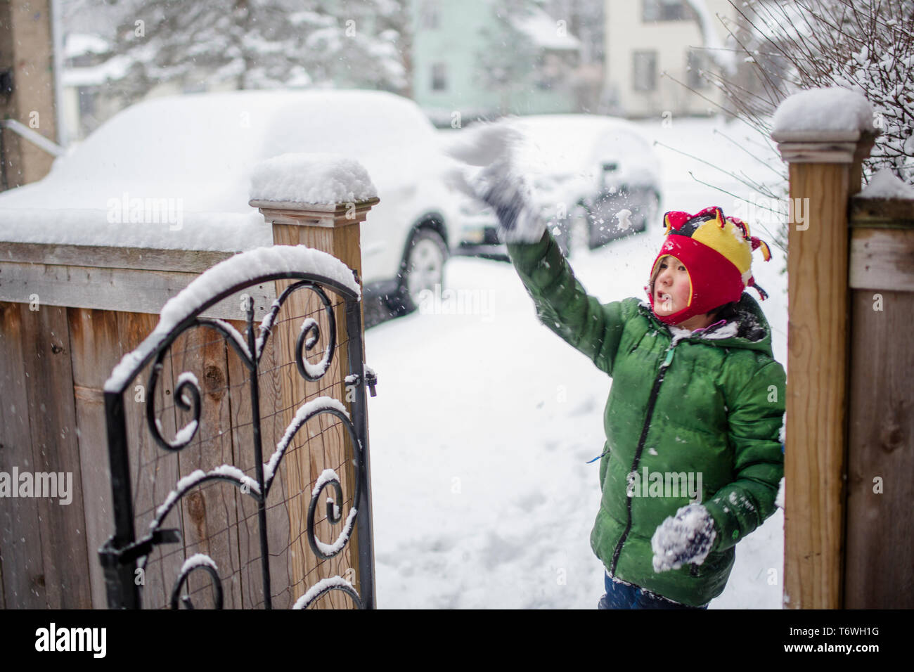 Portrait of a small boy by a gate playing in falling snow Stock Photo
