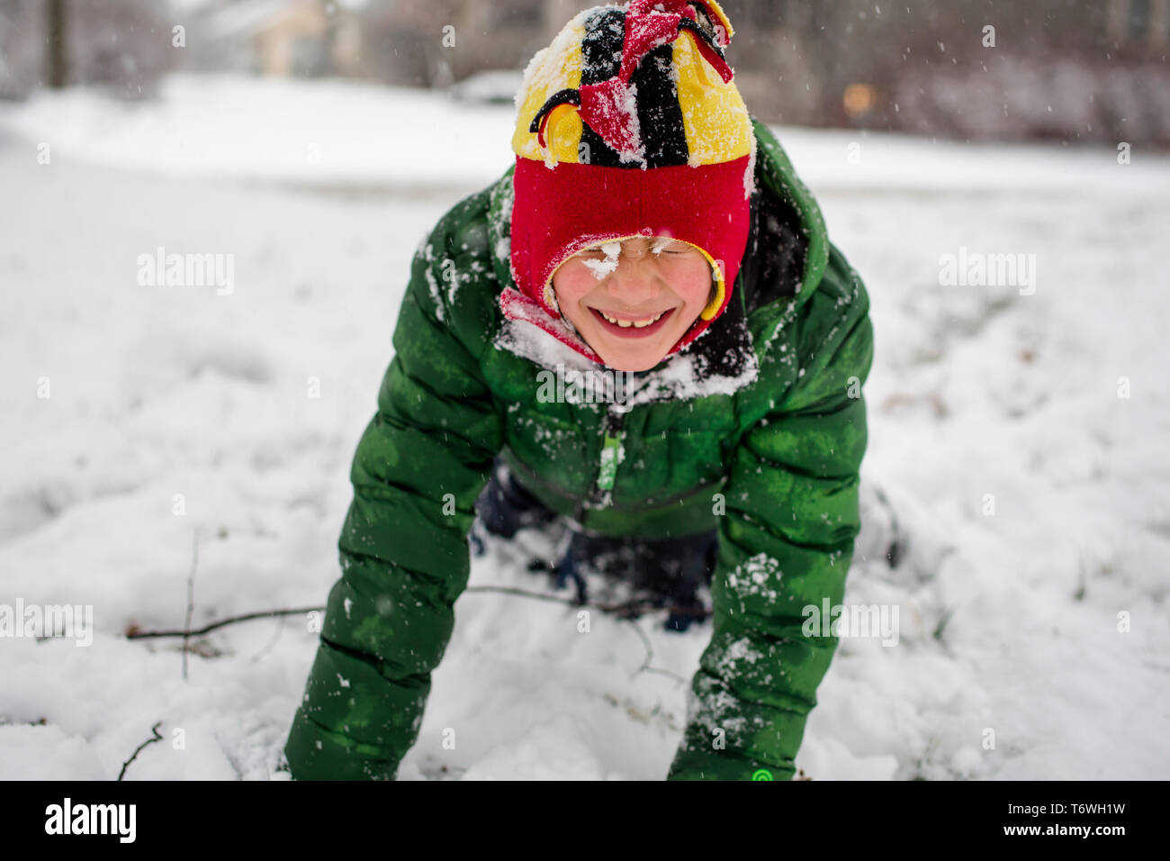 A small snow-covered child in fuzzy hat plays happily in snow Stock Photo