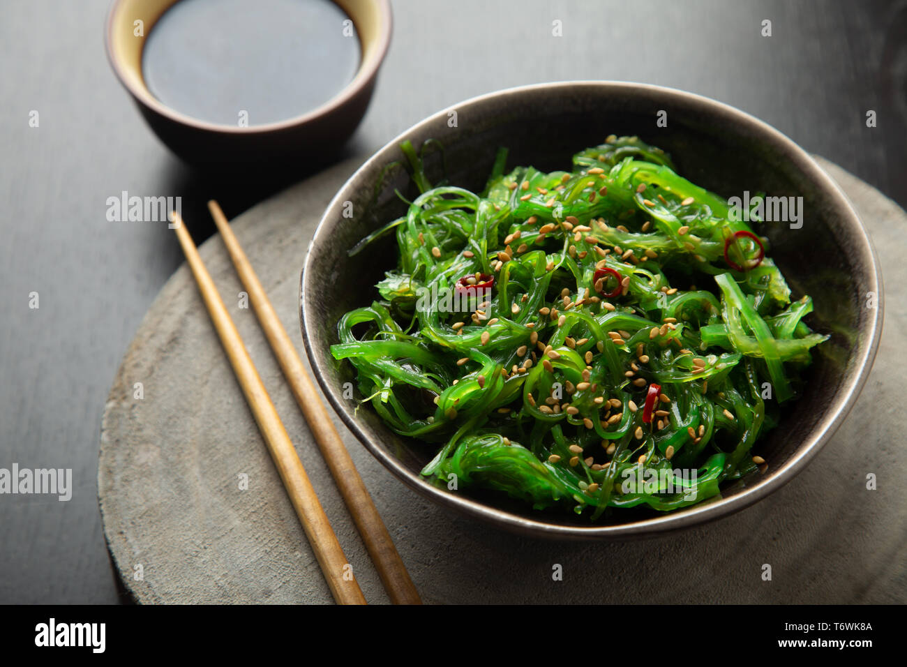 Wakame seaweed salad with sesame seeds and chili pepper in a bowl on a wooden slice Stock Photo