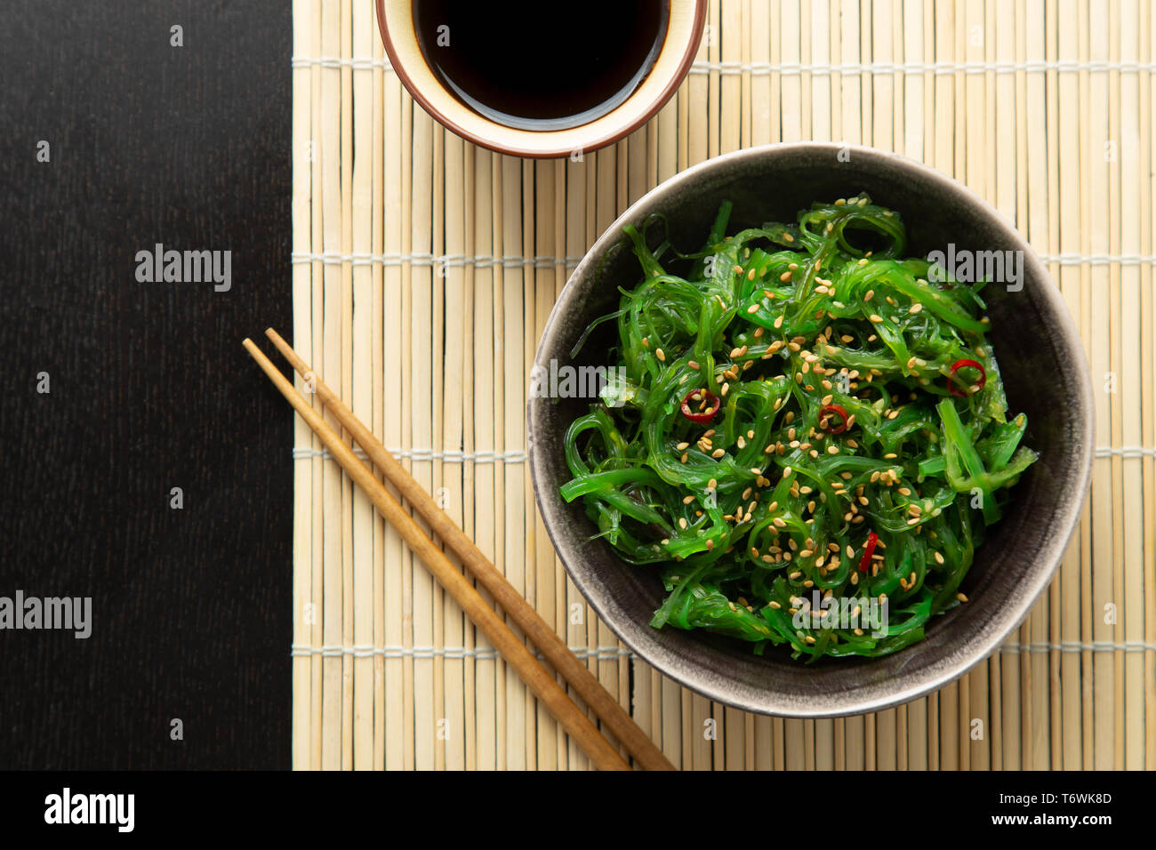 Wakame seaweed salad with sesame seeds and chili pepper in a bowl on a bamboo mat Stock Photo