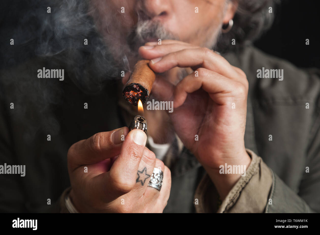 Closeup of hands of a middle aged man lighting up a cigar with a lighter, studio shot Stock Photo