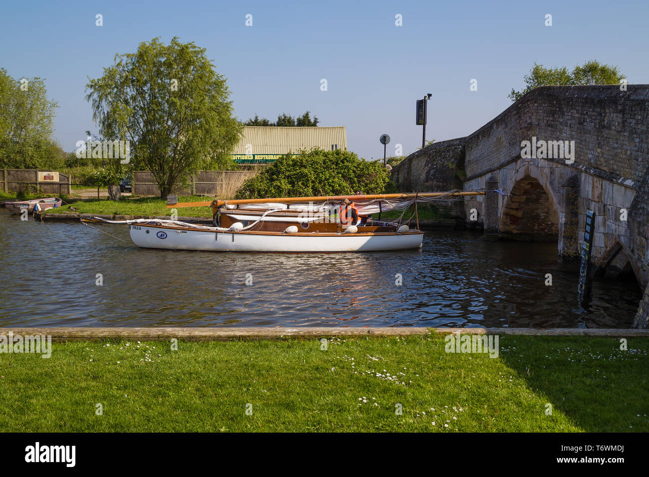 A boat with a retracted mast on the River Thurne navigates through a