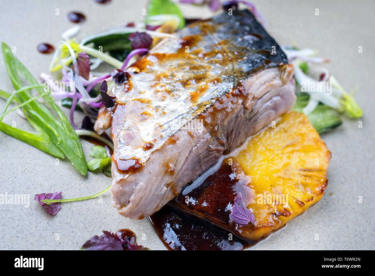 Modern style Japanese bonito tuna fish filet with vegetable and pineapple glazed in teriyaki sauce as closeup on a plate Stock Photo