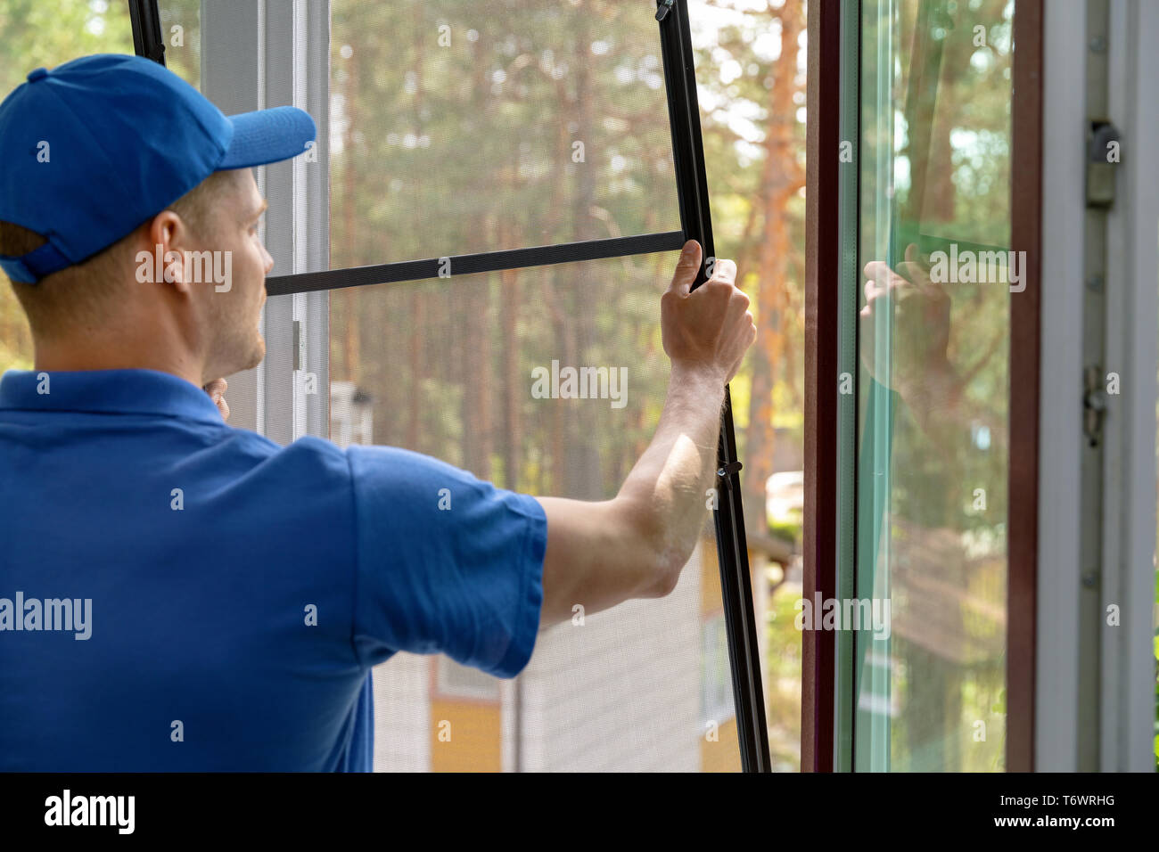 worker installing mosquito net wire mesh in plastic window frame Stock Photo