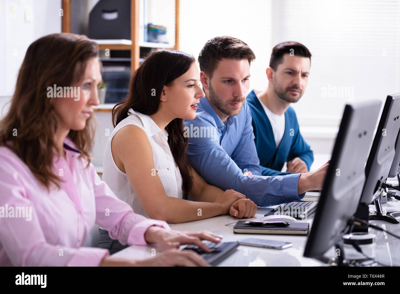 Businessman Pointing On Computer Screen While Talking With Her Colleague Stock Photo