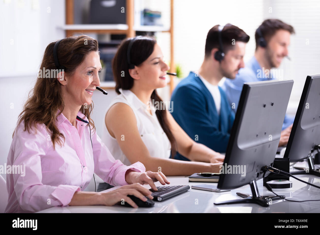 Happy Young Customer Service Executives Using Earphones Working In Call Center Stock Photo