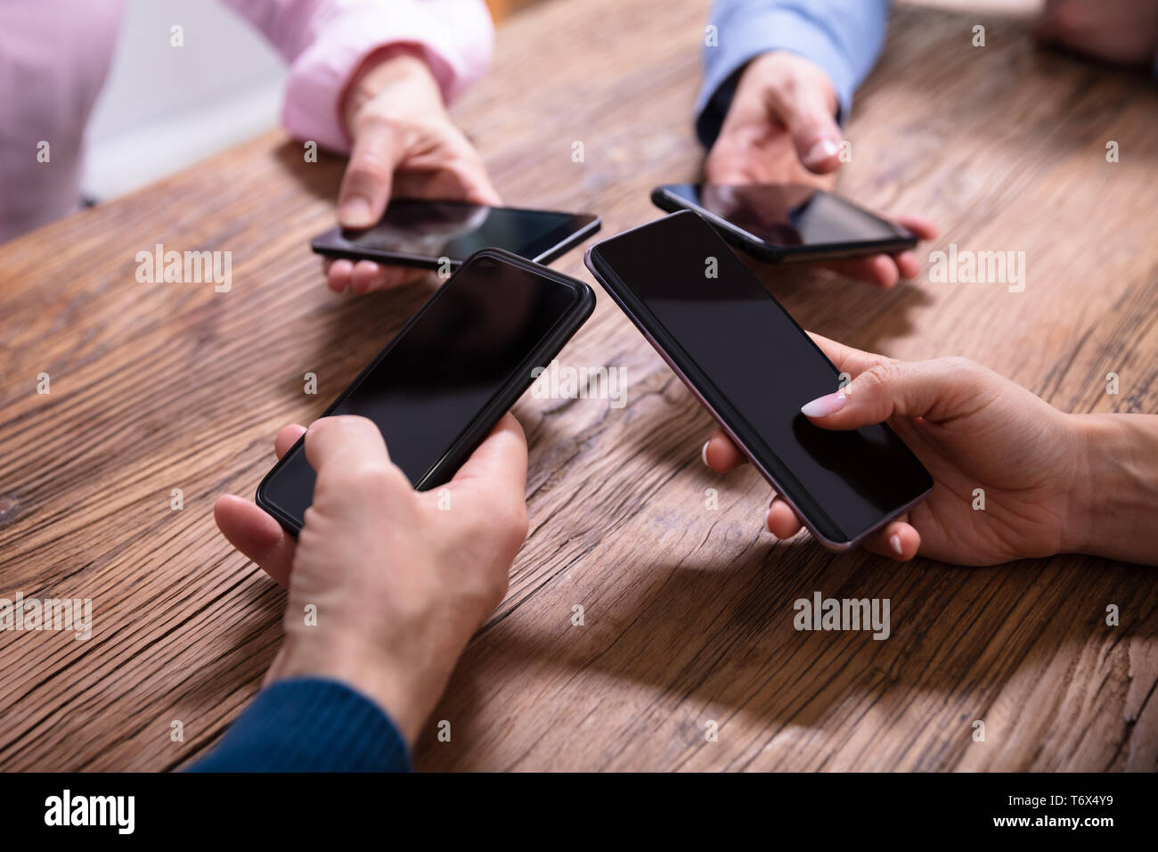 Close-up Of Businesspeople Using Mobile Phones Over Wooden Desk Stock Photo