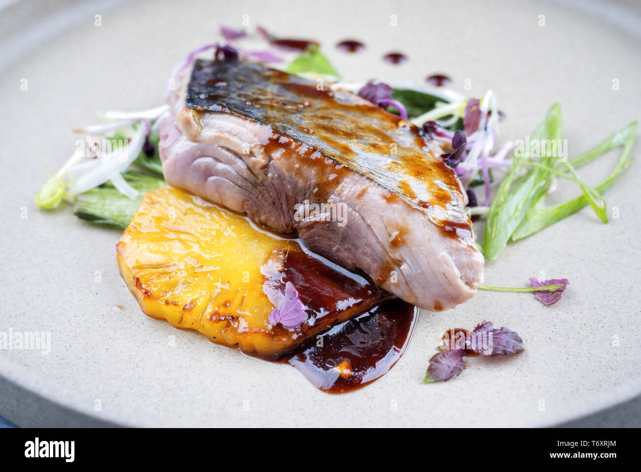 Modern style Japanese bonito tuna fish filet with vegetable and pineapple glazed in teriyaki sauce as closeup on a plate Stock Photo