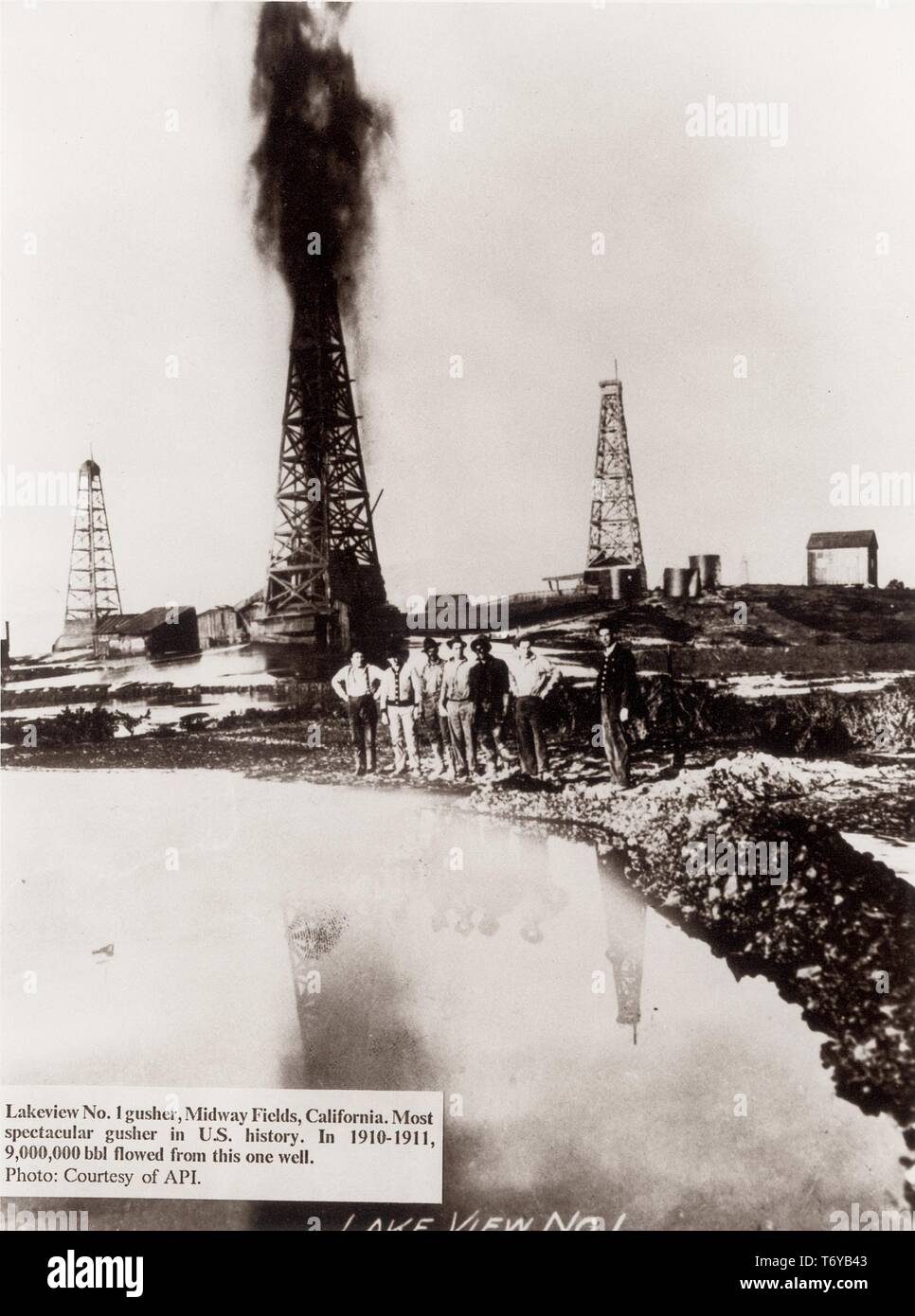 Workers stand at the edge of an open oil slick while Lakeview Gusher Number One explodes from a derrick in the background, Midway-Sunset Oil Field, California, 1910. Image courtesy American Petroleum Institute/US Department of Energy. () Stock Photo