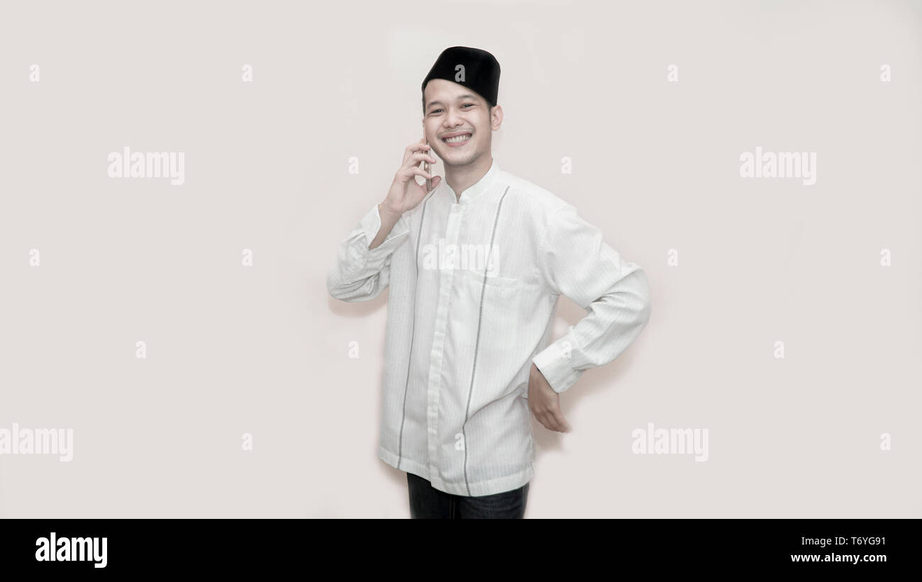 portrait of Funny an asian muslim man with head cap and baju koko taking a call for two way comunication -image Stock Photo