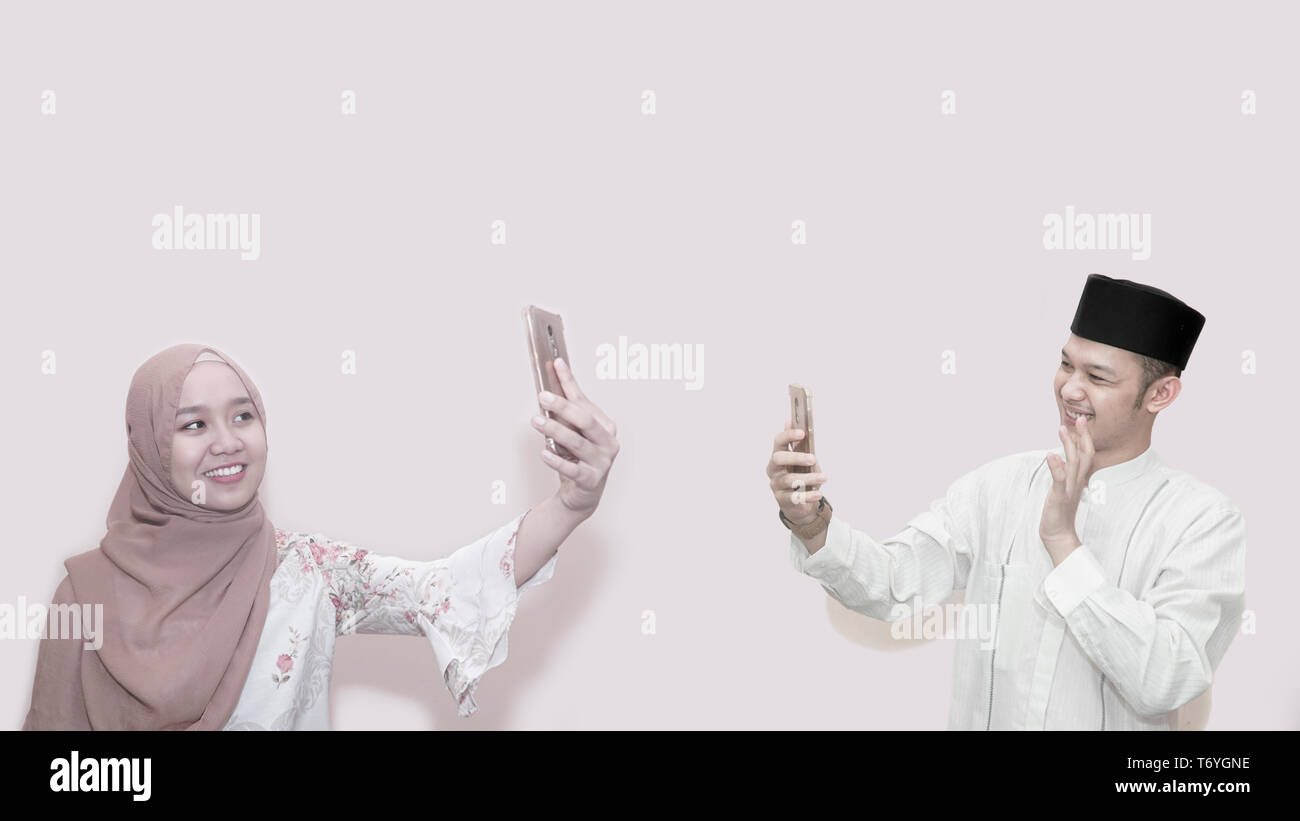 Portrait of asian muslim woman wearing head scarf or hijab and handsome male using smartphone to video call each others Stock Photo