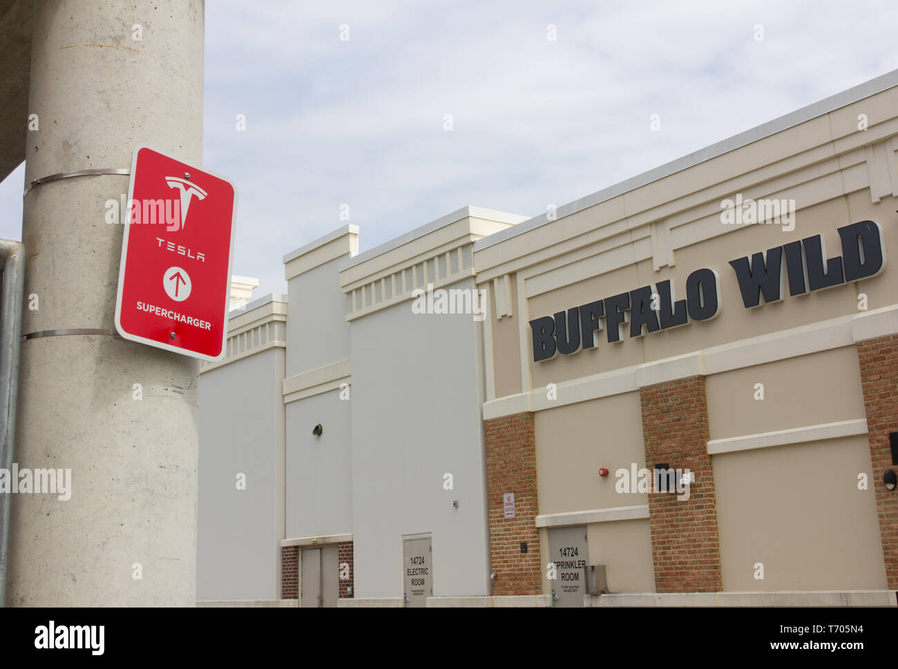 Pictured in April 2019 with a lopped Buffalo Wild Wings restaurant and the backs of stores in the background at the Towne Centre at Laurel shopping center/centre in Laurel, Maryland, USA, is a red 'Tesla Supercharger' sign with logo on a pillar of the parking garage/multi-storey car park where charging stations are located for the California-based automotive company's electric vehicles. The same month, a Tesla Model S caught fire at a Shanghai, China car park due to a faulty battery module in the car. As of June 2019, Tesla had more than 1,500 Supercharger stations worldwide. Kay Howell/Alamy Stock Photo