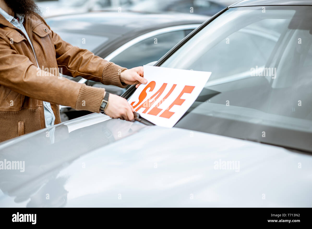Salesperson putting sale plate on the car windshield on the open ground of a dealership, close-up view Stock Photo