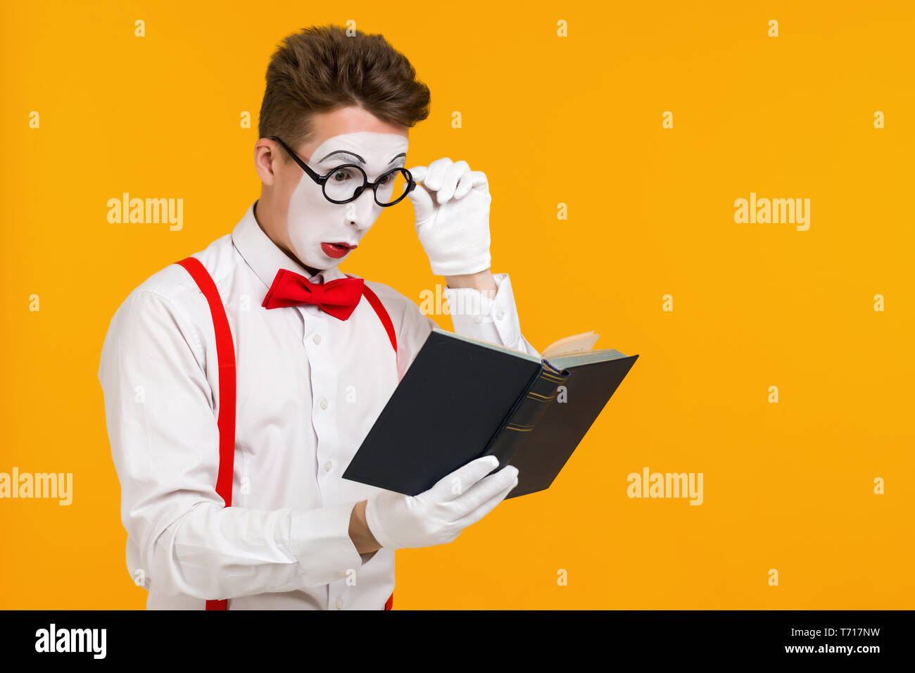 portrait of mime man artist reading book isolated on yellow background. copy space for text Stock Photo
