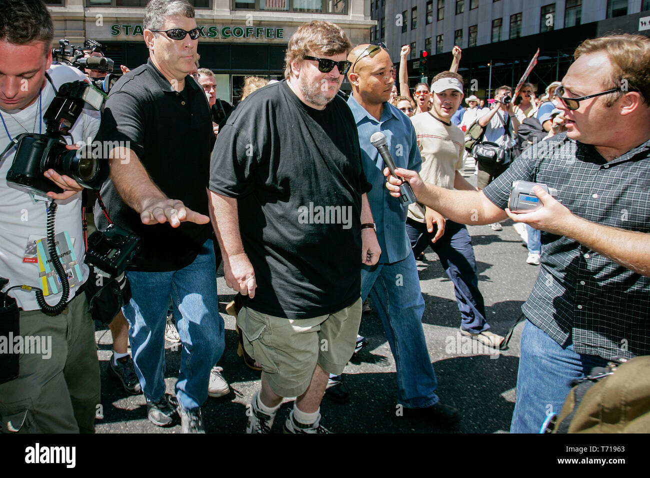 Documentary film maker and author Michael Moore is escorted by bodyguards while attending a protest march during the Republican National Convention in New York. To the left of Moore, shock jock and conspiracy theorist Alex Jones is trying to interview Moore. Stock Photo