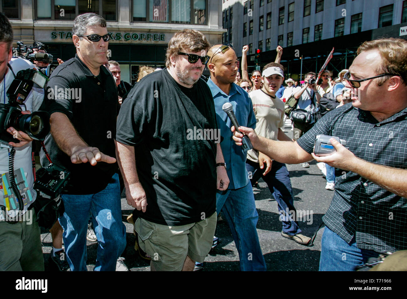 Documentary film maker and author Michael Moore is escorted by bodyguards while attending a protest march during the Republican National Convention in New York. To the left of Moore, shock jock and conspiracy theorist Alex Jones is trying to interview Moore. Stock Photo