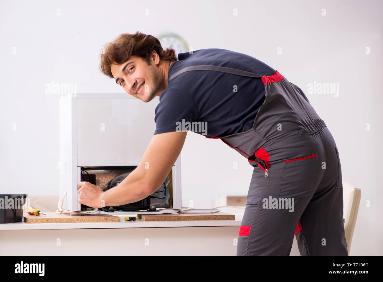 Young handsome contractor repairing fridge Stock Photo