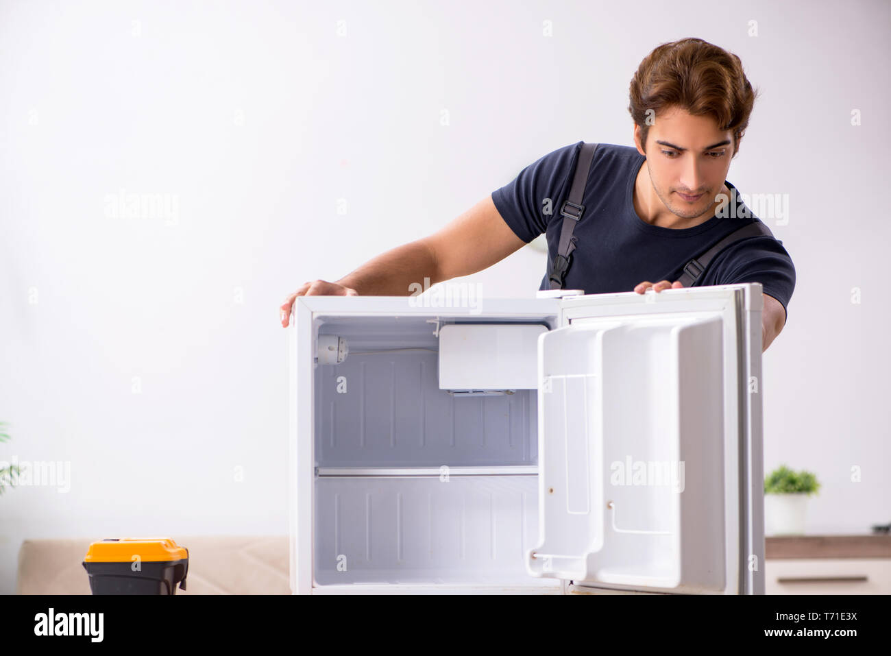 Young handsome contractor repairing fridge Stock Photo