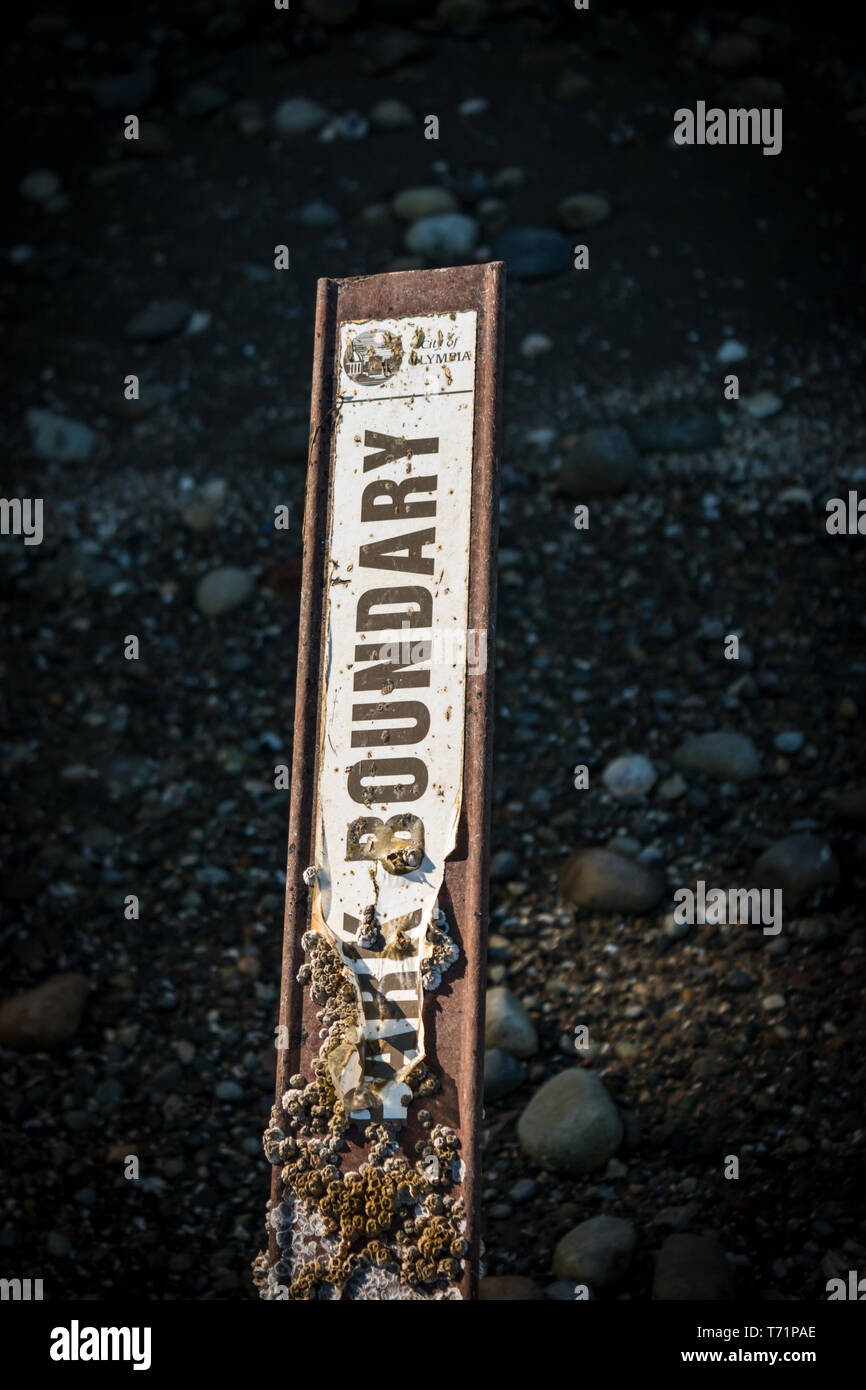 A park boundary sign partially covered in barnacles in Priest Point Park in Olympia, WA. Stock Photo