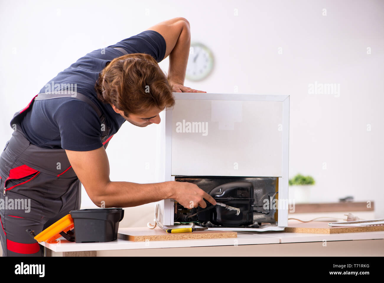 Young handsome contractor repairing fridge Stock Photo
