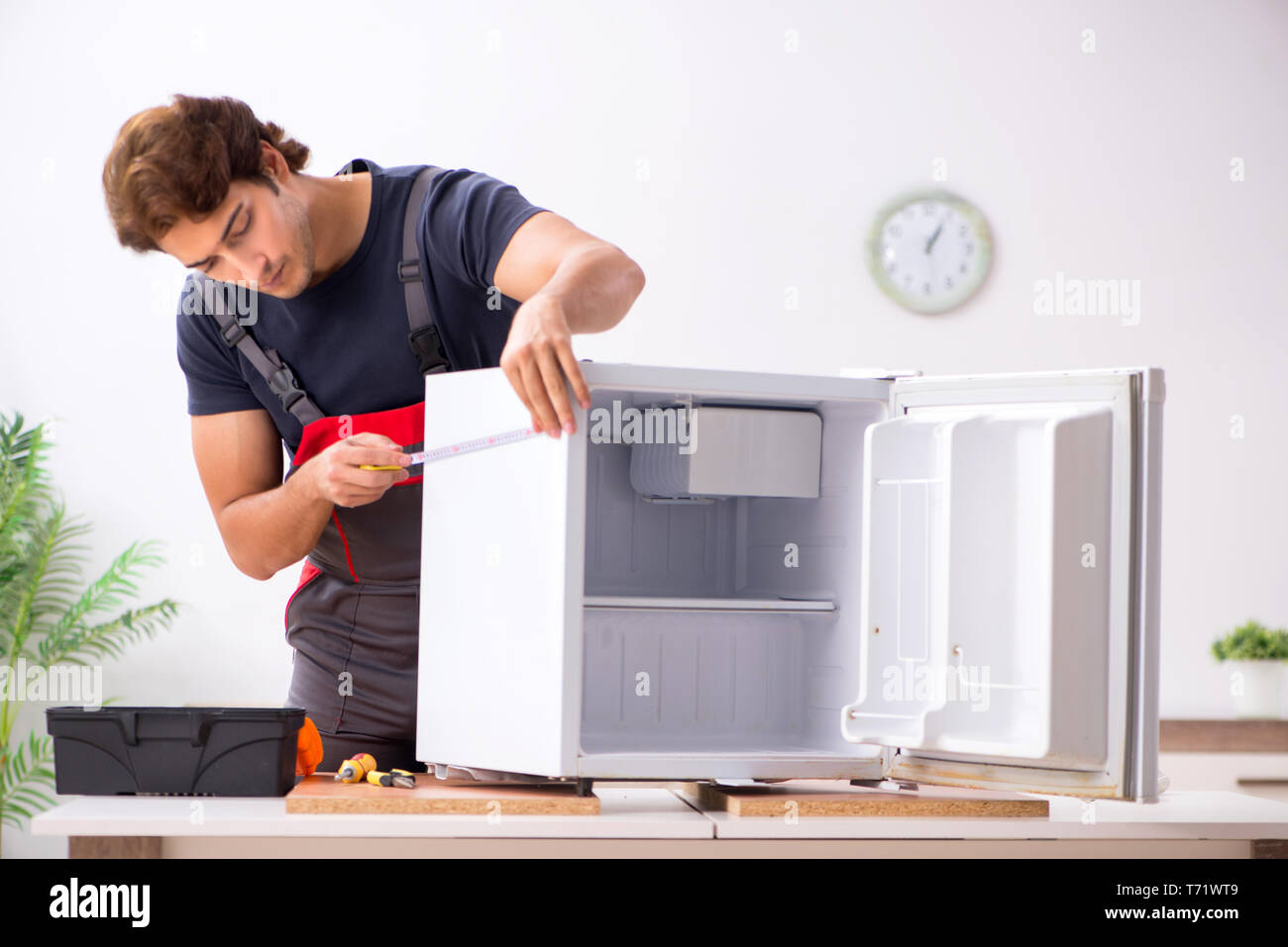 Young handsome contractor repairing fridge Stock Photo