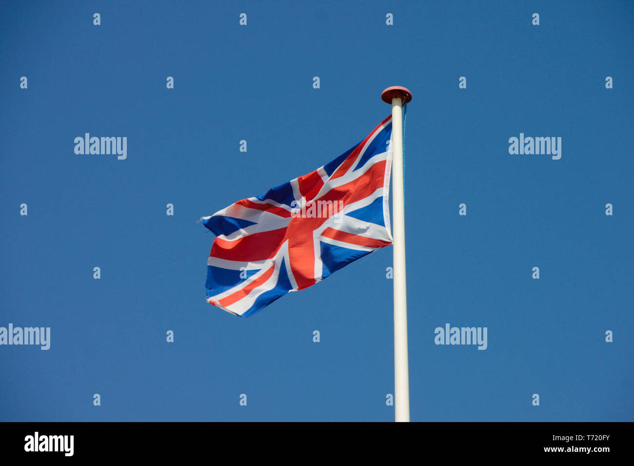 Union Jack, flag of the united kingdom flapping in the wind. Blue sky in the background. Stock Photo