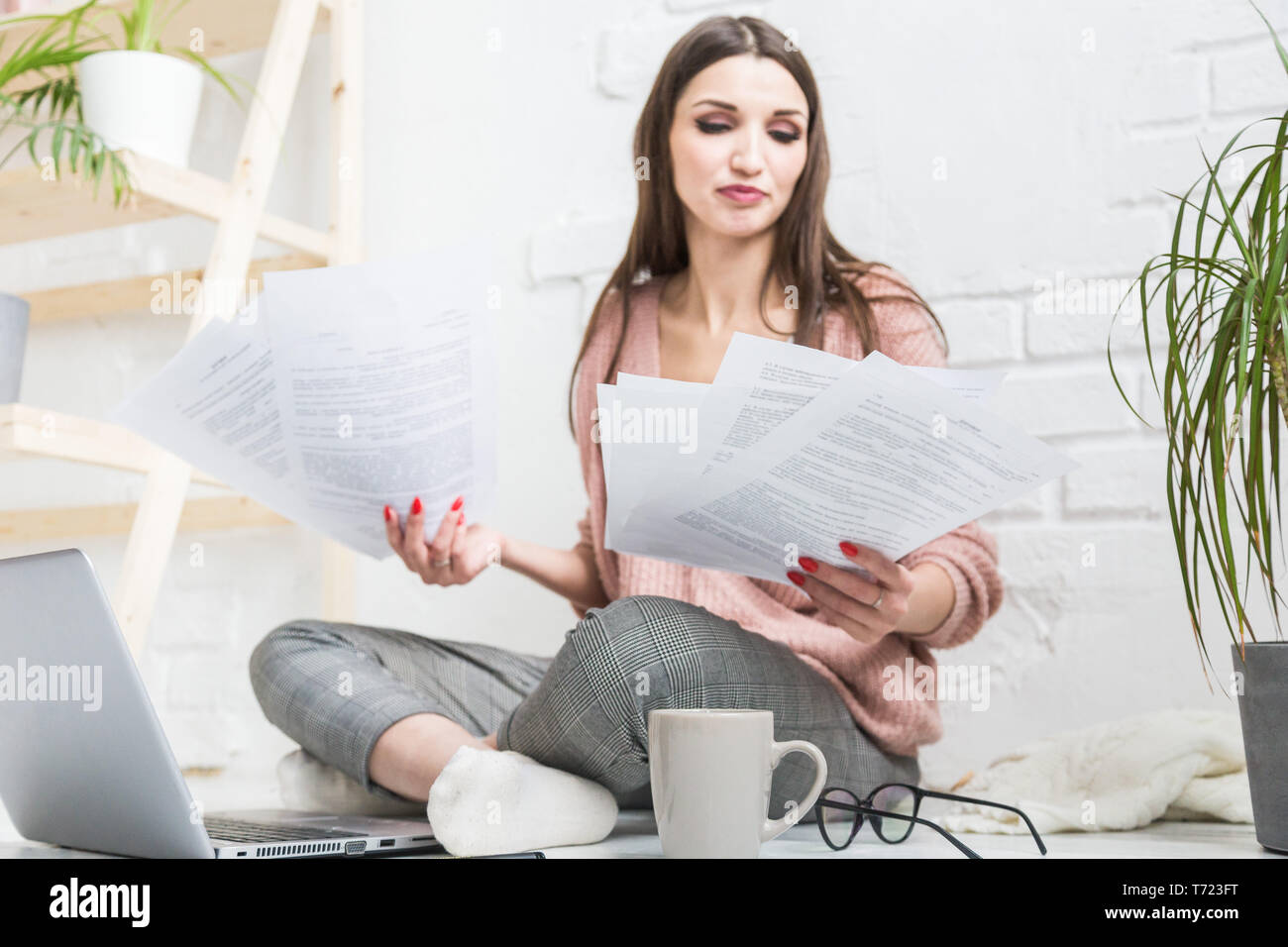 Happy woman examines the paper sitting near the laptop, the girl freelancer works with documents. Student girl gets education remotely using internet Stock Photo
