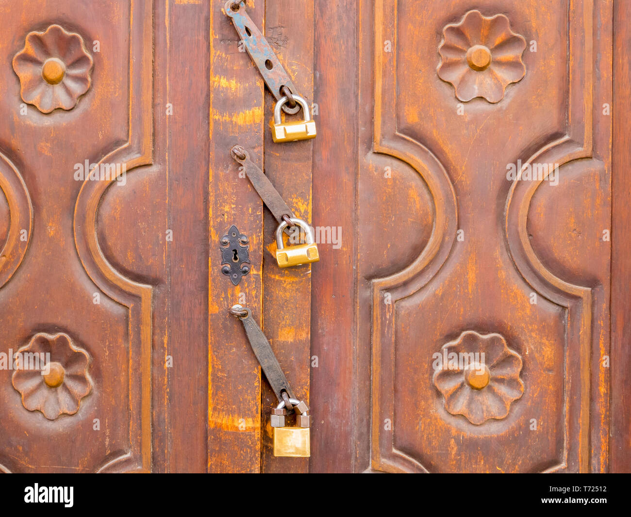 ancient wooden door closed with three padlocks Stock Photo
