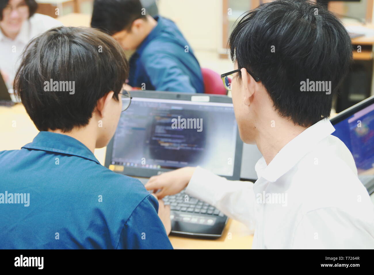 Two Thai computer engineering student discussing about the computer code in their project on a laptop during the class Stock Photo