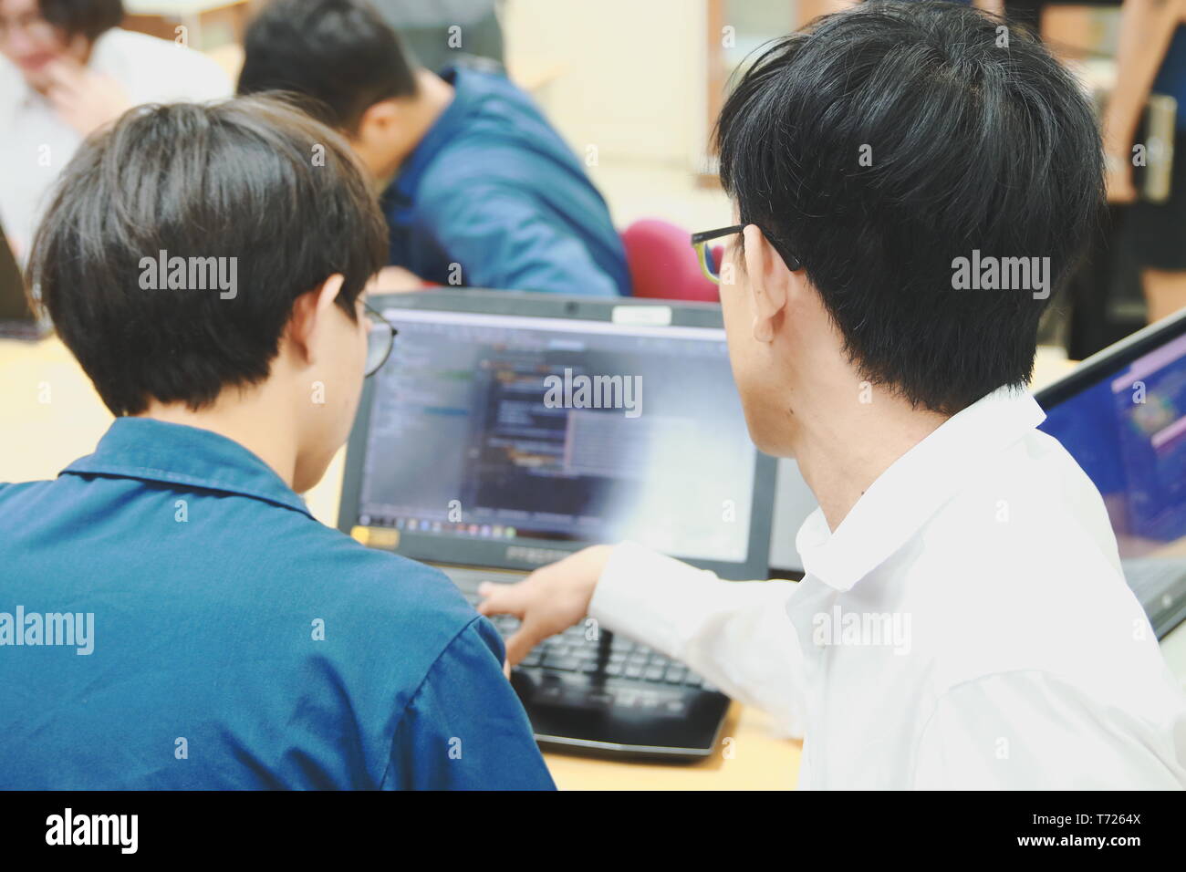 Two Thai computer engineering student discussing about the computer code in their project on a laptop during the class Stock Photo