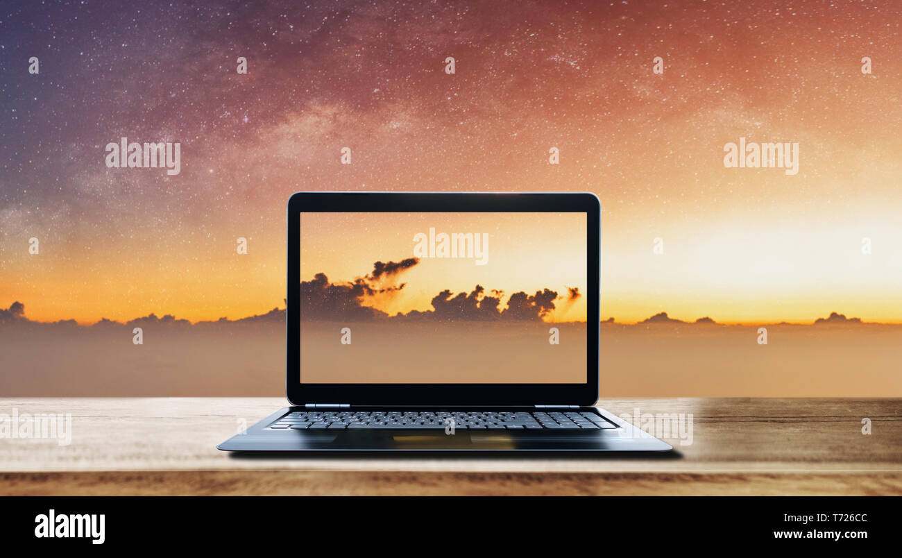Computer laptop on wooden desk and sunrise sky with stars background ...