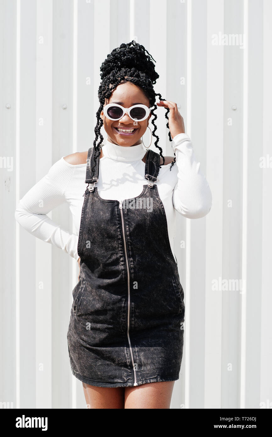 African woman in denim overalls skirt white sunglasses posed
