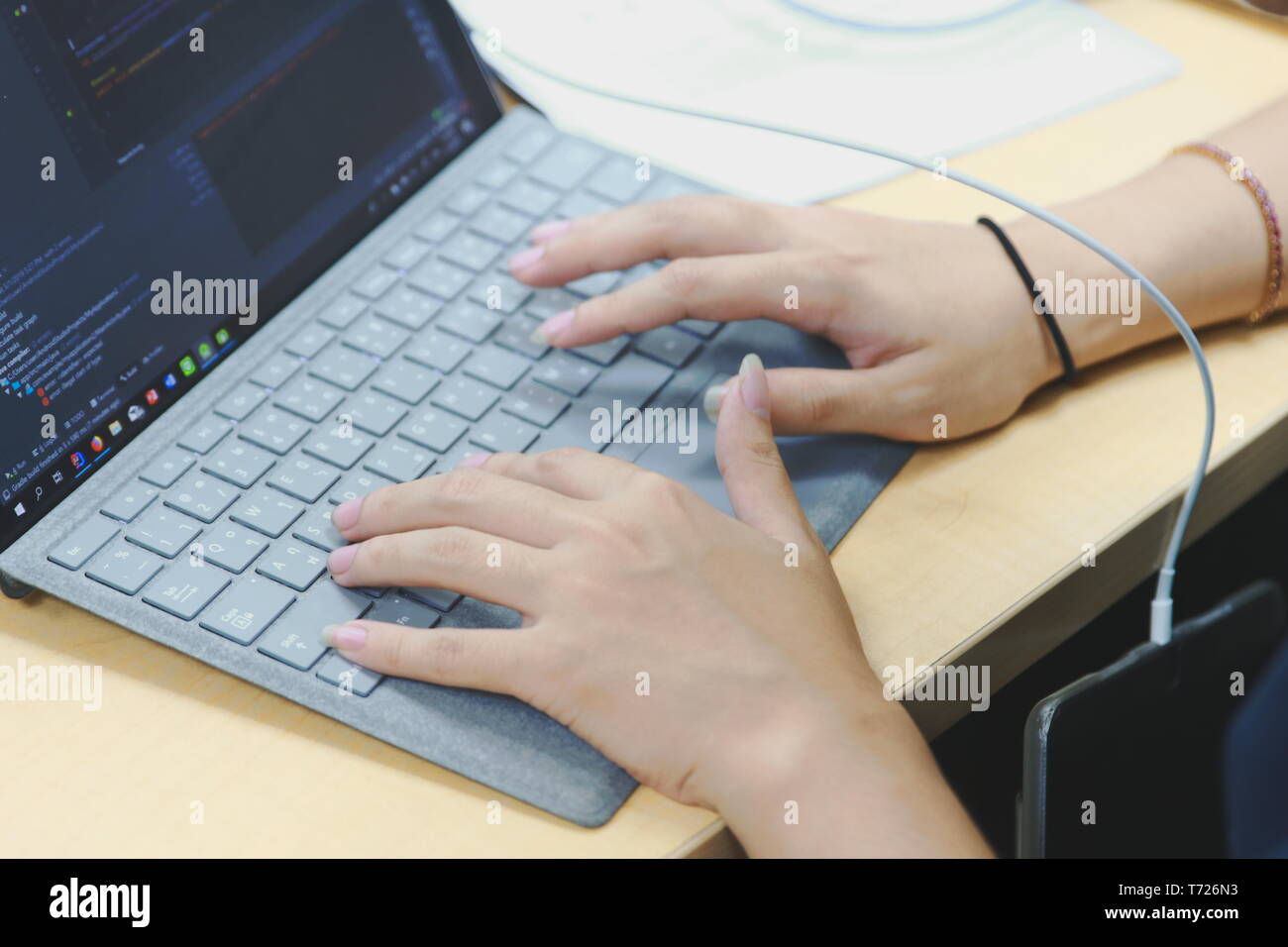 Close up of a hand typing on a Microsoft Surface Pro keyboard with his phone hanging on USB cable while charging Stock Photo