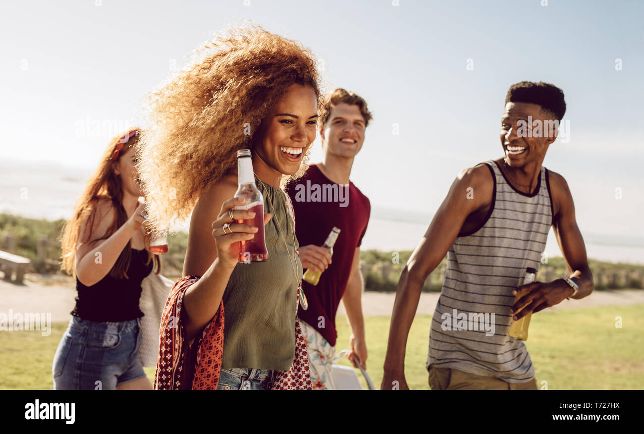 Attractive woman having beer while walking with friends outdoors. Female hanging out with group of friends on a summer day. Stock Photo