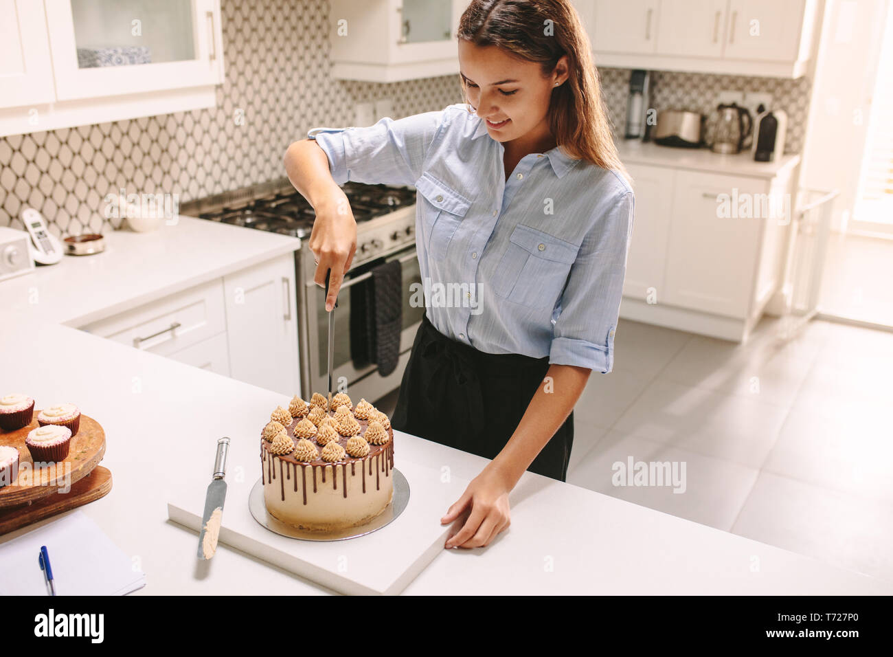 Female chef cutting freshly prepared cake in the kitchen. Woman pastry chef cutting a cake. Stock Photo
