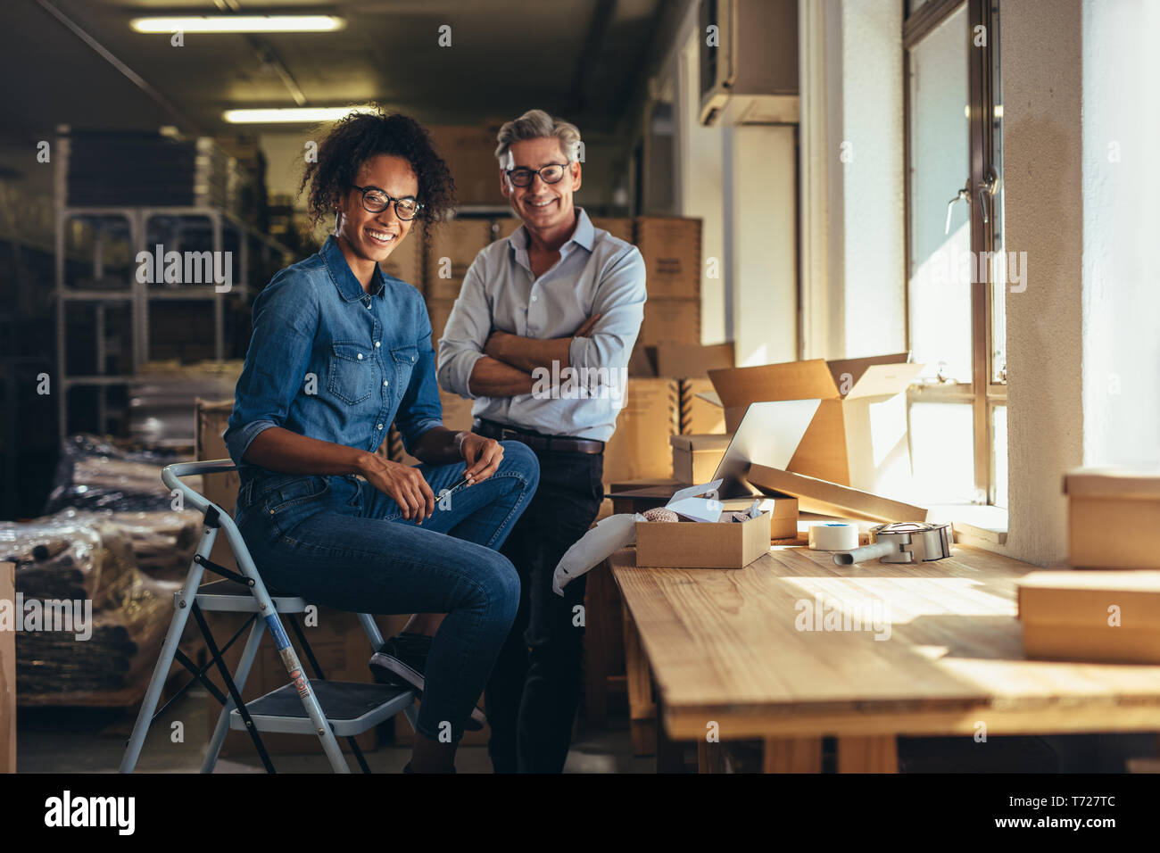 Smiling business partners together at online seller warehouse. Young woman and mature man looking at camera and smiling at drop shipping business offi Stock Photo